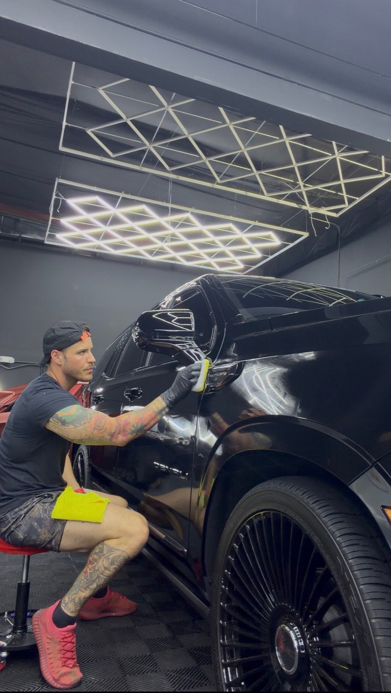 Minty detailer applying protection to a black pickup under workshop lights